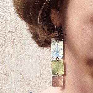 Può includere: Orecchini rettangolari in tonalità argento, oro e rame con una texture martellata.