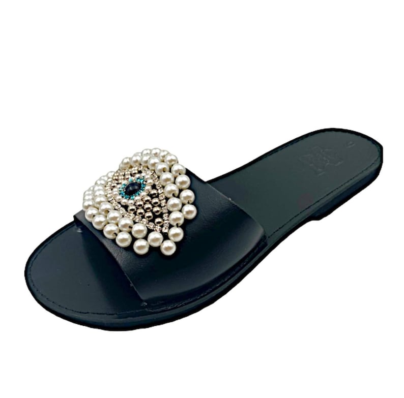 May include: Black leather slide sandals with a pearl and crystal embellished evil eye design.