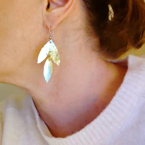 Puede incluir: Pendientes de hoja de oro con textura martillada. Los pendientes son colgantes y tienen forma de lágrima.