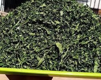 May include: A large pile of dried green leafy vegetables in a green plastic container.