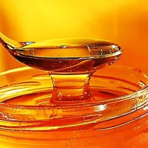 May include: A close-up of a glass jar filled with honey. A spoon is dipping into the honey, and the honey is dripping from the spoon.