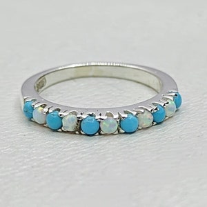 Op de afbeelding: Een zilveren bandring met afwisselende turquoise en witte opaalstenen.
