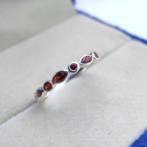 May include: A silver band ring with a row of red gemstones. The gemstones are oval shaped and set in a silver band.
