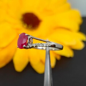 May include: A silver ring with a red oval gemstone and small clear stones set in the band.