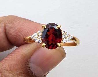 May include: A gold ring with a large oval-shaped red gemstone surrounded by smaller white gemstones.