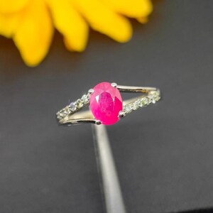 May include: A silver ring with a bright pink oval ruby gemstone and smaller clear gemstones set in the band.