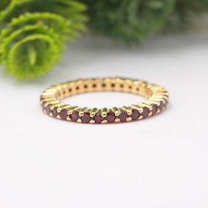 Può includere: Un anello a fascia d'oro con una fila di piccole pietre preziose rosse.