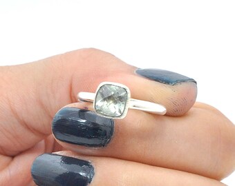 May include: A silver ring with a square-shaped clear gemstone. The ring is on a finger with dark blue nail polish.