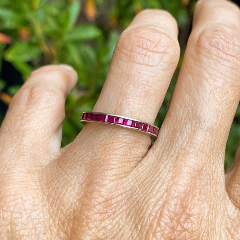 May include: A thin gold band ring with a row of small, square-shaped ruby stones.