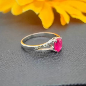 May include: A silver ring with a bright pink oval gemstone and smaller clear gemstones on the band.