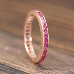 Może przedstawiać: Złota obrączka z różowego złota z rzędem różowych szafirów osadzonych w ciągłym okręgu.