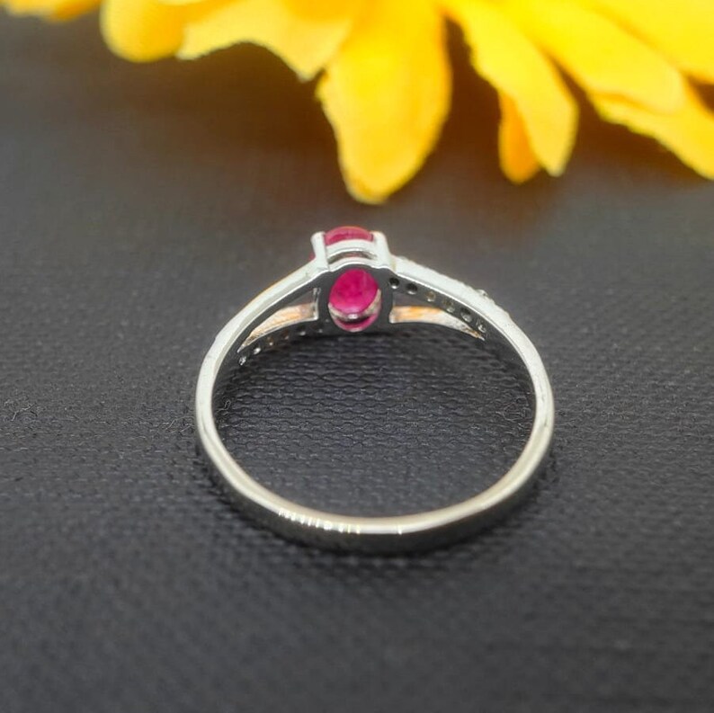 May include: A silver ring with a red oval gemstone and small clear stones set in the band.
