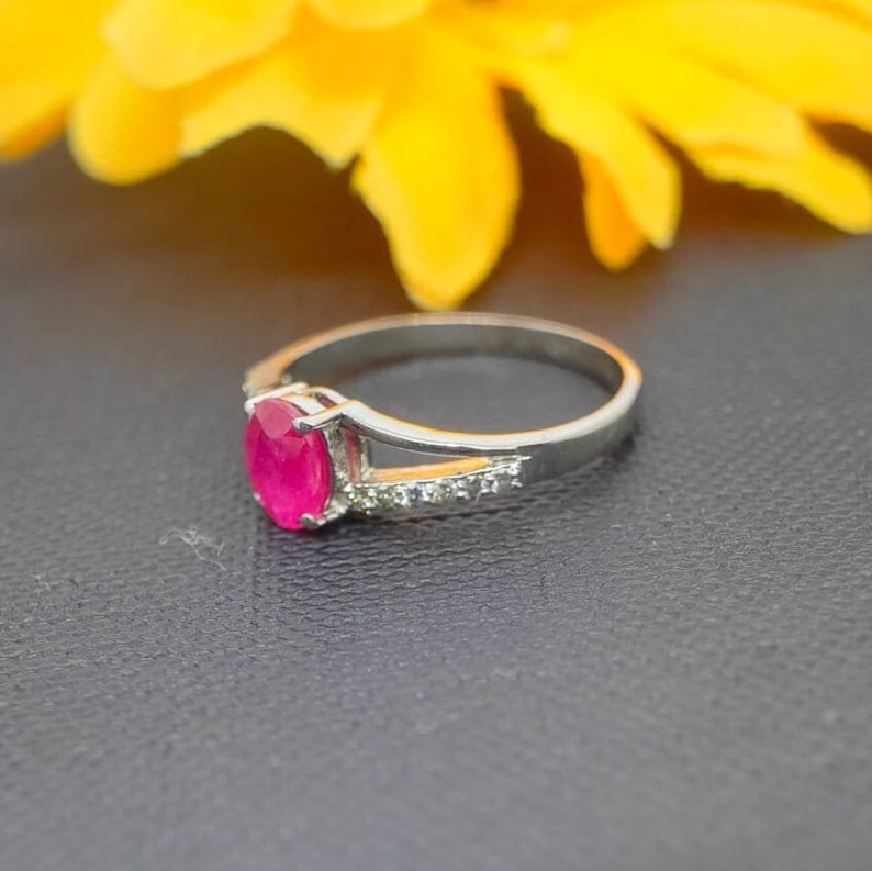 May include: A silver ring with a pink oval gemstone and smaller clear gemstones set in the band.