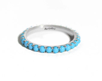 May include: A silver band ring with a row of turquoise blue stones around the entire band. The ring is engraved with the words "Rings of Memory".
