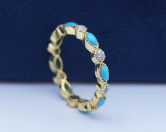 May include: A gold ring featuring alternating turquoise and diamond-like stones. The turquoise stones are marquise-shaped, and the ring has a delicate, elegant design. The ring is set against a blue background.