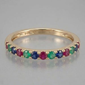 May include: A gold band ring with alternating gemstones of red, green, and blue. The ring is marked with "14K" and features a polished finish. The gemstones are evenly spaced around the band.