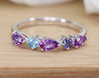 Puede incluir: Un anillo de banda de plata con una fila de piedras preciosas de colores. El anillo presenta una amatista en forma de lágrima, una topacio azul redonda y piedras más pequeñas de amatista y topacio azul.