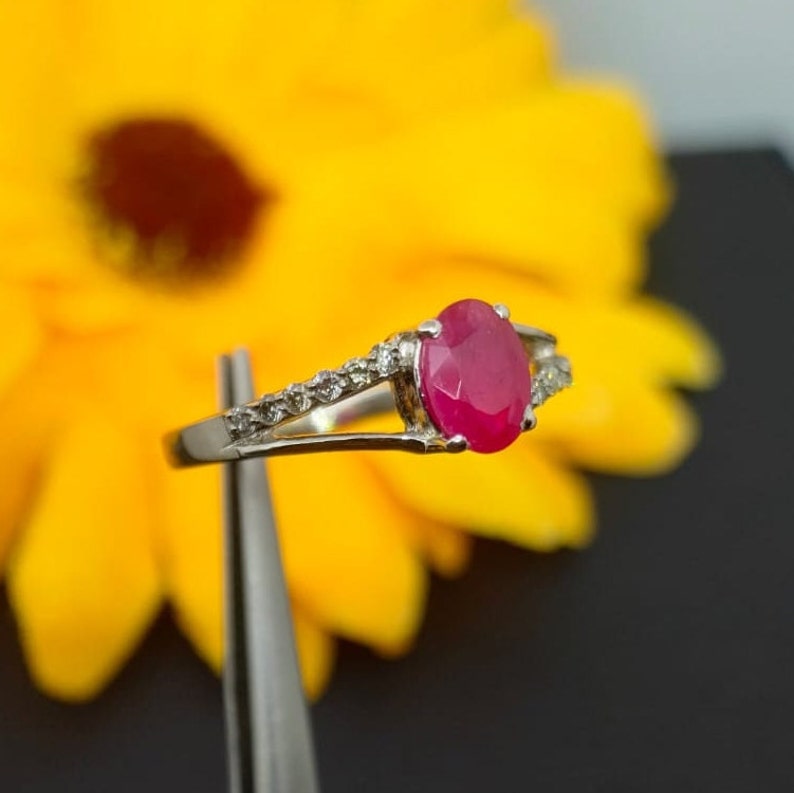 May include: A silver ring with a large oval-shaped ruby gemstone and smaller diamonds set in the band.