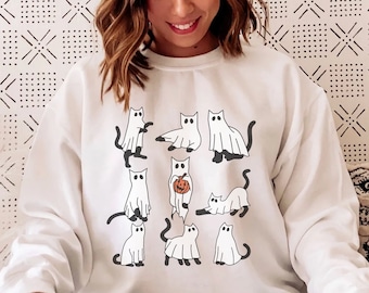 May include: White sweatshirt with a graphic print of multiple black cats dressed as ghosts. Some cats are holding pumpkins.