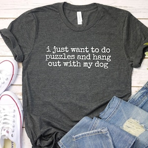 May include: A dark gray t-shirt with the text "i just want to do puzzles and hang out with my dog" printed in white on the front.