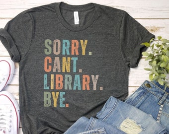 Może przedstawiać: Szary t-shirt z napisem "SORRY. CANT. LIBRARY. BYE." w kolorowych, dużych literach. Litery są przetarte i mają vintage'owy wygląd.