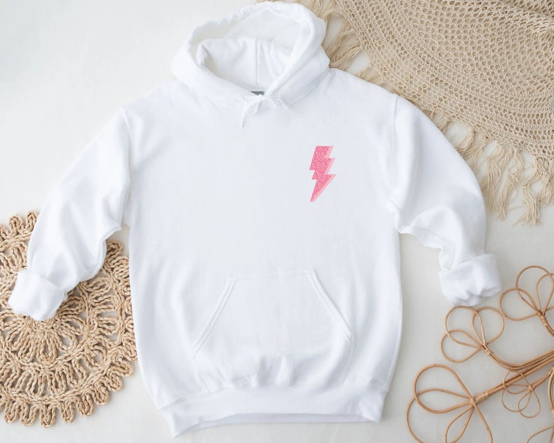 May include: White hoodie with a pink glitter lightning bolt graphic on the front.