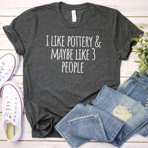 May include: A dark gray t-shirt with the text "I like pottery & maybe like 3 people" printed in white.