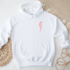 K&ouml;nnte beinhalten: Wei&szlig;er Kapuzenpullover mit einem pinkfarbenen Blitz-Motiv auf der Vorderseite.