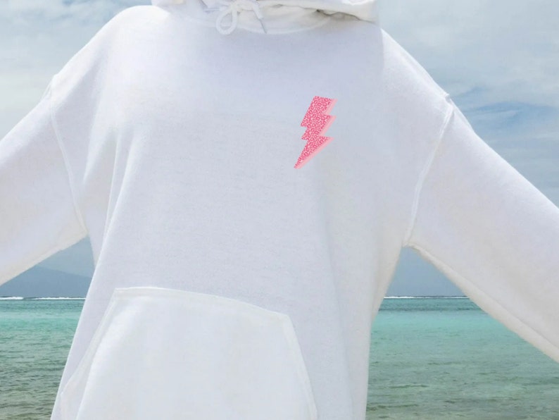 May include: White hoodie with a pink glitter lightning bolt design on the front.