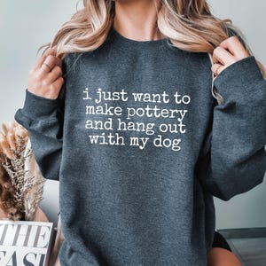 May include: A dark gray sweatshirt with the text "i just want to make pottery and hang out with my dog" printed in white.