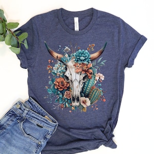 Puede incluir: Una camiseta azul marino con un dise&ntilde;o floral que presenta una calavera de vaca blanca con cuernos. Las flores son en tonos de azul, naranja y verde.