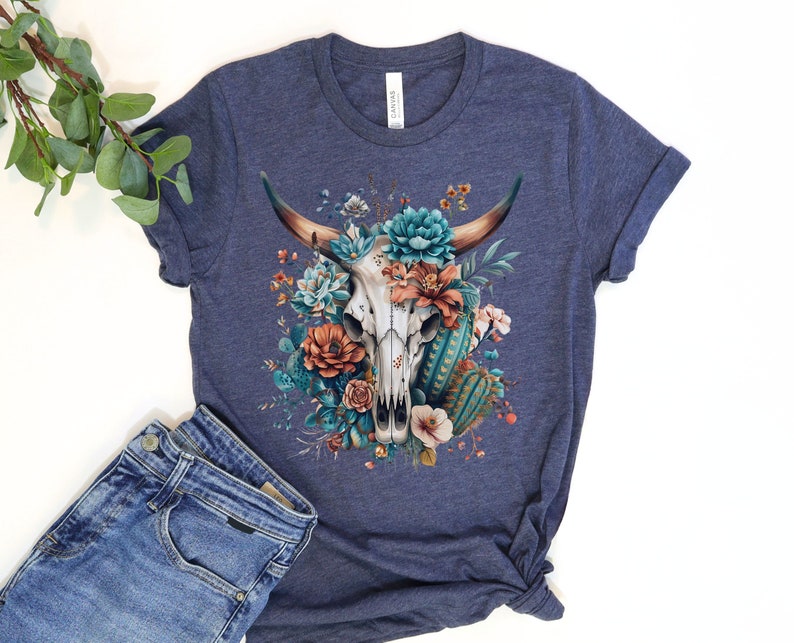 Puede incluir: Una camiseta azul marino con un dise&ntilde;o floral que presenta una calavera de vaca blanca con cuernos. Las flores son en tonos de azul, naranja y verde.
