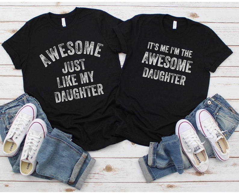 May include: Two black t-shirts with white text. The first shirt says "Awesome Just Like My Daughter". The second shirt says "It's Me I'm The Awesome Daughter".