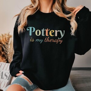 May include: Black sweatshirt with the text "Pottery is my therapy" in rainbow colors.