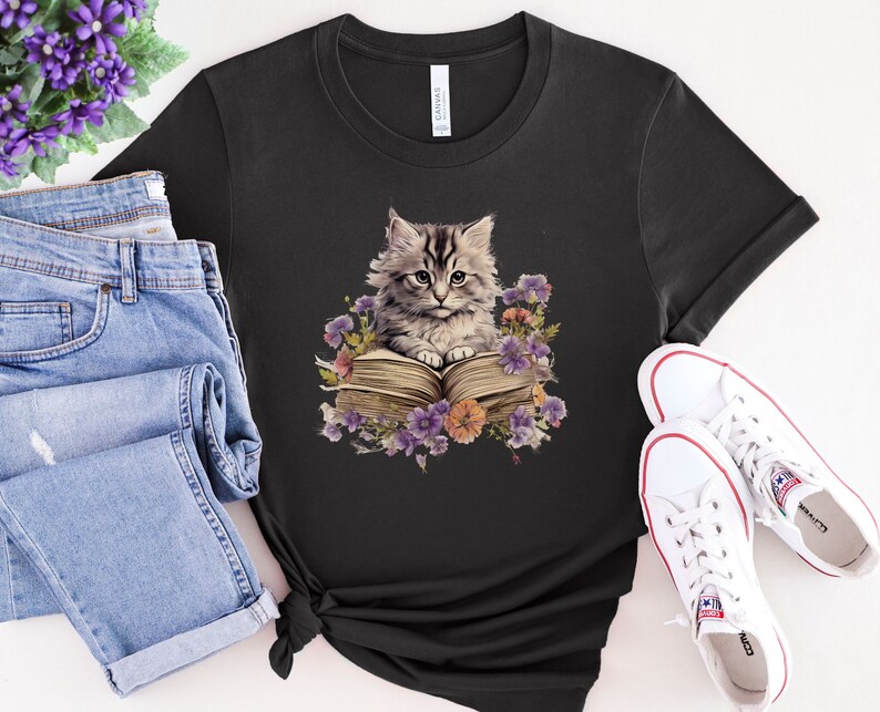 May include: A black t-shirt with a graphic of a gray and white kitten sitting on a book surrounded by purple, pink, and yellow flowers.