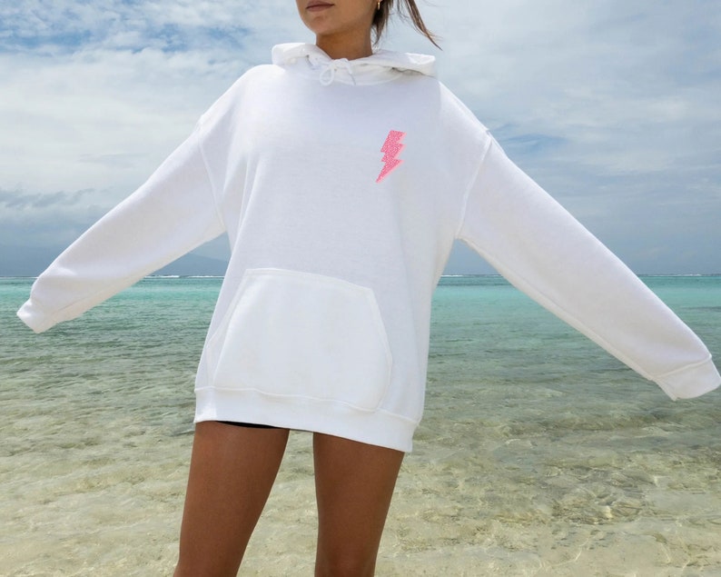 a woman in a white hoodie standing on a beach