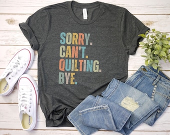 May include: A dark gray t-shirt with the text "SORRY. CAN'T. QUILTING. BYE." in colorful retro-style lettering.