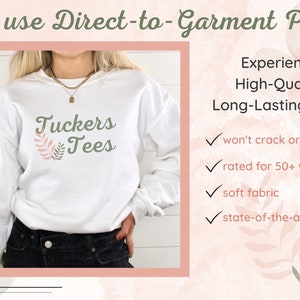 May include: White sweatshirt with the text "Tuckers Tees" and a green leaf design. The text "We use Direct-to-Garment Print" is at the top of the image. The text "Experience High-Quality, Long-Lasting Prints" is on the right side of the image. Below the text are four check marks with the following text: "won't crack or peel", "rated for 50+ washings", "soft fabric", and "state-of-the-art print".