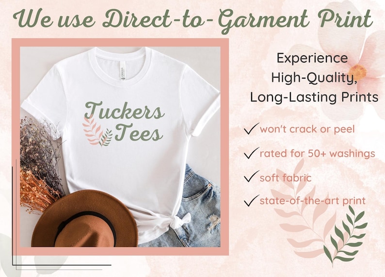 Peut inclure: Un t-shirt blanc avec un motif floral vert et rose et le texte "Tuckers Tees". L'image montre le t-shirt sur une table avec un chapeau marron et un jean bleu. Le texte "We use Direct-to-Garment Print" est en haut de l'image. Le texte "Experience High-Quality, Long-Lasting Prints" est &agrave; droite de l'image. Sous le texte, il y a quatre coches avec le texte suivant : "won't crack or peel", "rated for 50+ washings", "soft fabric", et "state-of-the-art print".