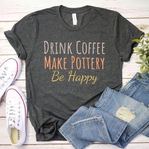 May include: A gray t-shirt with the text "Drink Coffee Make Pottery Be Happy" in white and orange lettering.