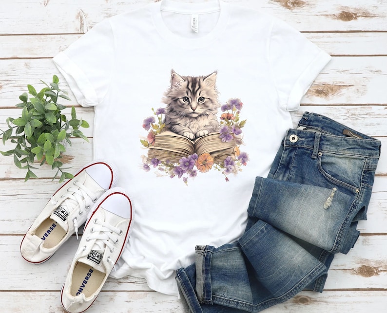 May include: White t-shirt with a graphic of a cat reading a book surrounded by flowers.