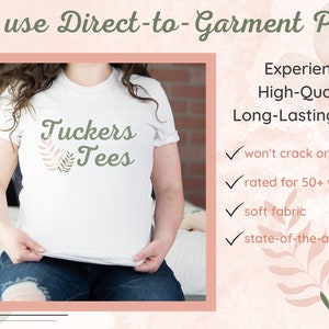 Puede incluir: Camiseta blanca con el texto "Tuckers Tees" y un dise&ntilde;o floral verde y rosa. El texto "We use Direct-to-Garment Print" est&aacute; en la parte superior de la imagen. El texto "Experience High-Quality, Long-Lasting Prints" est&aacute; en el lado derecho de la imagen. Una marca de verificaci&oacute;n est&aacute; junto a cada uno de los siguientes: "won't crack or peel", "rated for 50+ washings", "soft fabric", y "state-of-the-art print".