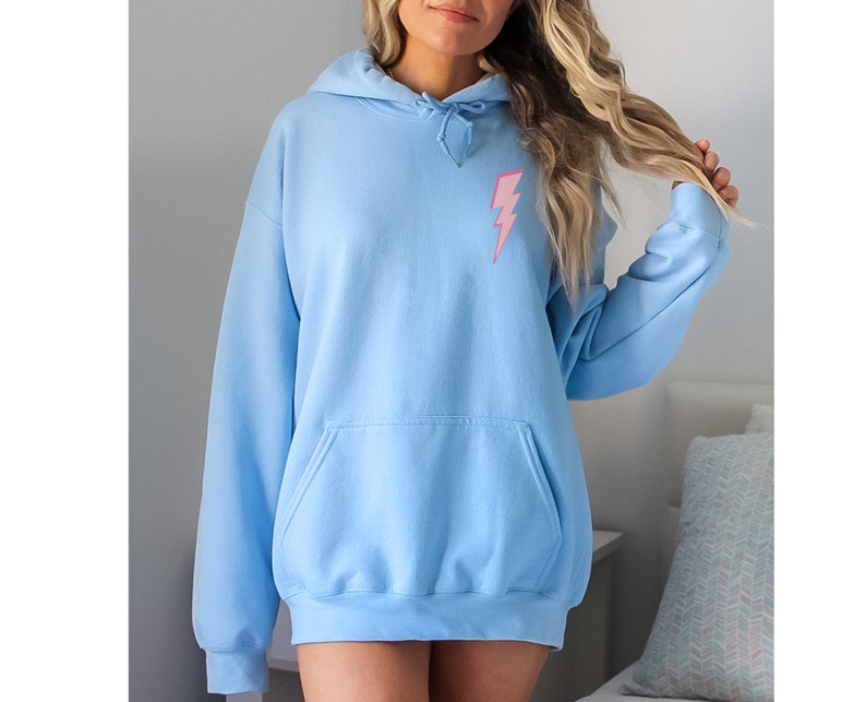 Puede incluir: Una sudadera de color azul claro con un gr&aacute;fico de rayo rosa en la parte delantera.