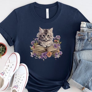 May include: A navy blue t-shirt with a graphic of a gray cat sitting on an open book surrounded by purple flowers.