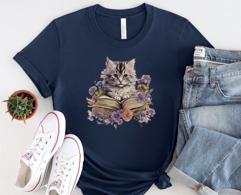 May include: A navy blue t-shirt with a graphic of a gray cat sitting on an open book surrounded by purple flowers.