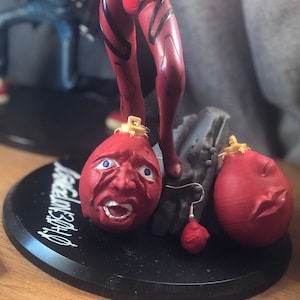 Könnte beinhalten: Eine rote und schwarze Anime-Figur, die auf einem schwarzen Sockel mit drei roten und weißen Gesichtsornamenten steht. Der Sockel trägt die Aufschrift "Remarkable".