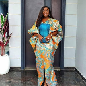 May include: A floor-length kaftan dress featuring a vibrant orange and metallic blue marbled pattern with wide, voluminous sleeves. The garment includes a solid teal blue rectangular panel on the chest and a central front slit at the hemline.
