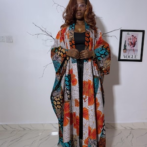 Puede incluir: Una colorida bata estilo kimono estampada con diseños florales y geométricos en naranja, azul y negro. La bata está abierta por delante y se lleva sobre un conjunto negro. En el fondo se ve una portada enmarcada de la revista Vogue.