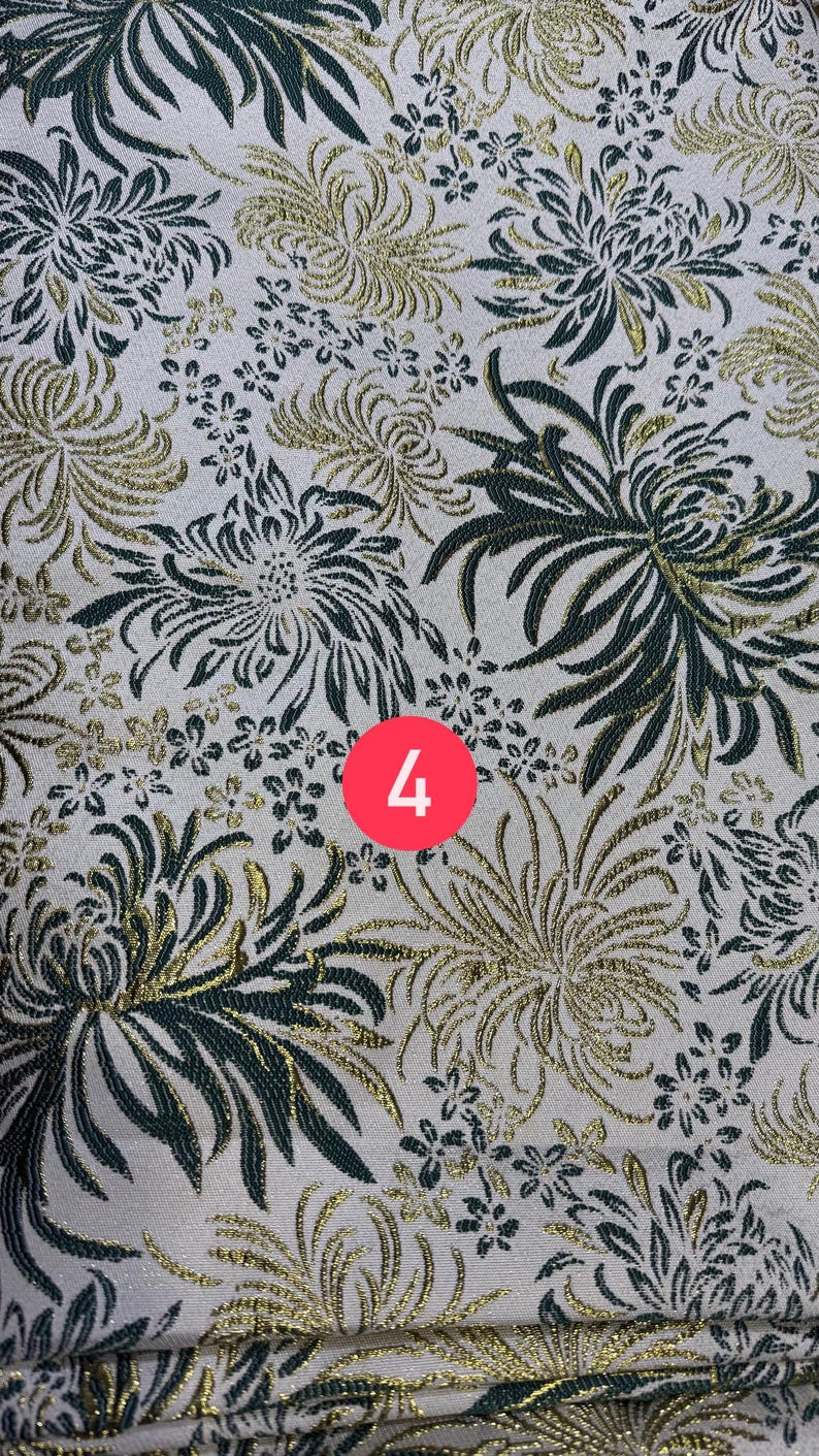 May include: A fabric featuring a repeating pattern of dark green and metallic gold chrysanthemum flowers on a light cream background. A circular red icon with the white number 4 is positioned in the center of the textile design.