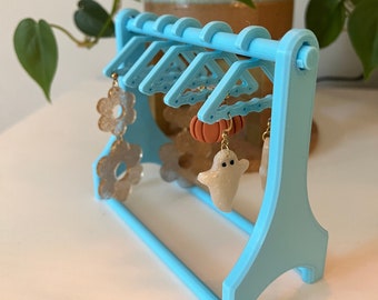 May include: A light blue earring display stand with five hangers. The stand has a small shelf and is decorated with Halloween-themed earrings, including a ghost, a pumpkin, and flowers.